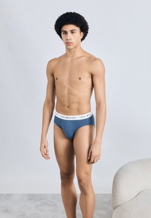 Slip in blauwe stof met een witte tailleband met merknaam. Soepele textuur en strakke pasvorm, met een minimalistische stijl.