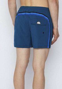 Pantaloncini da bagno blu con cintura, strisce nere e blu a contrasto sui lati e una tasca posteriore con un dettaglio a patta arrotondata.
