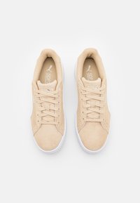 Sneaker in suede beige con suole in gomma bianca, caratterizzate da un design con lacci e logo PUMA sulla linguetta e sul lato. Texture liscia complessiva.