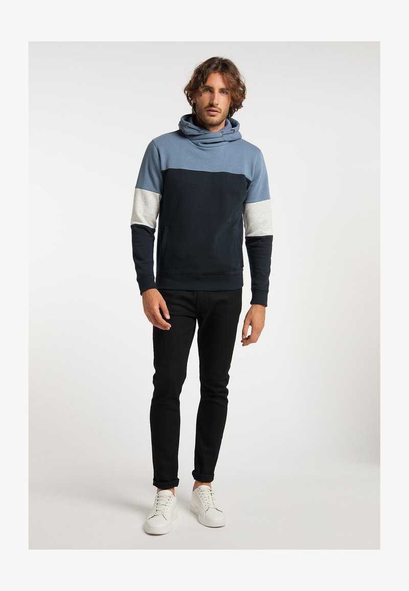 Laikku ja vaaleansininen huppari, jossa on kauluri, harmaat kontrastiväriset hihat ja miellyttävä pinta, yhdistettynä mustiin slim fit -housuihin ja valkoisiin lenkkitossuihin.