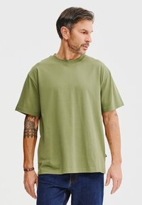 Oliwkowa bawełniana koszulka z okrągłym dekoltem i krótkimi rękawami, o luźnym kroju i minimalistycznym designie.