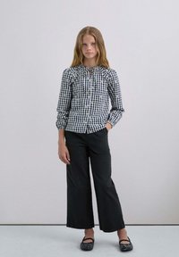 Camisa de manga larga a cuadros en blanco y negro con escote fruncido, combinada con pantalones anchos negros y zapatos planos negros con adornos.