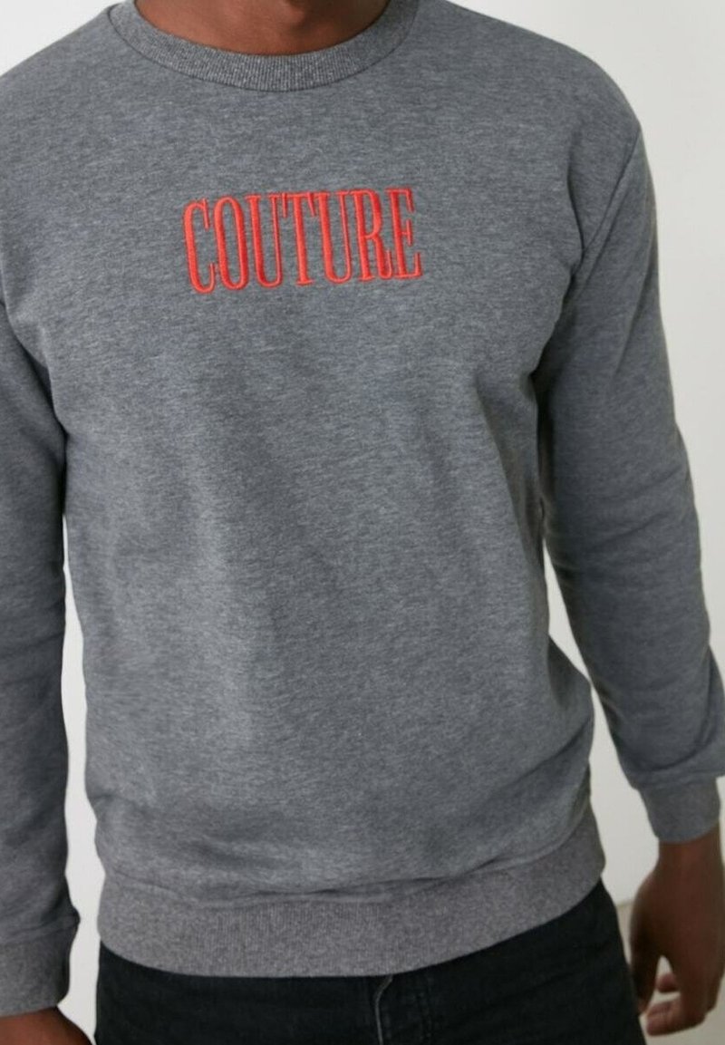 Sudadera gris con bordado rojo de "COUTURE". Presenta un cuello de barco y puños y dobladillo acanalados, fabricada con un tejido suave y texturizado.