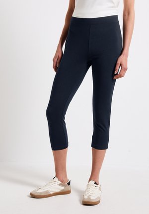 Navy cropped leggings i stretchmaterial med en mjuk textur och resårmidja, kombinerat med avslappnade sneakers.