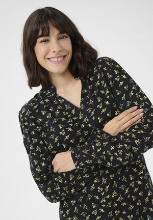 Blouse noire avec un motif floral jaune, manches longues et décolleté en V. Le tissu semble doux avec une texture lisse.