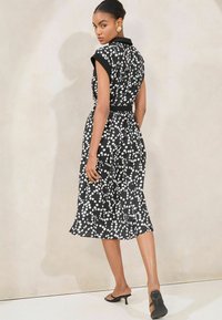 Rochie neagră cu model de puncte albe, talie ajustată, mâneci scurte și tiv la genunchi. Stilizată cu un curea neagră și saboți cu vârf deschis.
