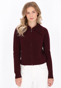 Burgunderfarbene Zip-up-Strickjacke mit strukturiertem Strickdesign, einem Kragen und gerippten Bündchen. Der Schnitt ist schmal und kontrastiert mit hellen Hosen.