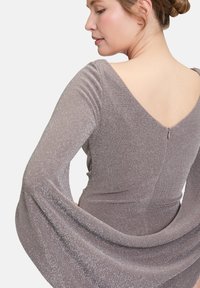 Robe à manches longues scintillante en tissu gris doux, présentant un dos en V profond et des manches fluides avec un corps ajusté et un zip au dos.