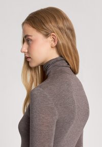 Maglione a maniche lunghe fitted con collo alto in un morbido tessuto a maglia marrone testurizzato. Collo alto con sottili dettagli delle cuciture, visto di lato.