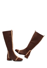 Botas marrones hasta la rodilla con parte superior de tela lisa y detalles en beige contrastante. Tacones cuadrados y punteras de ante que aportan textura y detalle.