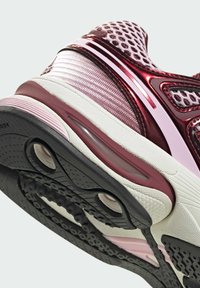 Baskets de sport avec une tige bordeaux brillante en mesh texturé, une semelle intermédiaire blanche et une semelle extérieure en caoutchouc noir à motifs avec amorti à air.