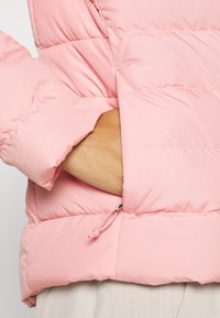 Veste en doudoune rose clair avec une texture matelassée, un cordon de serrage ajustable à l'ourlet et des manches à coupe décontractée.