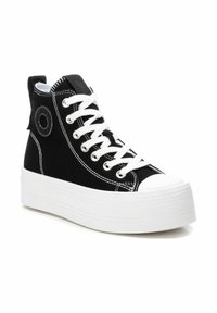 Zapatilla alta negra con suela de goma blanca, que presenta cordones blancos, acentos de costura y un logo circular en el lateral.