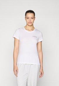 Biele tričko s krátkym rukávom a okrúhlym výstrihom, s malým potlačeným textom "ATHLEISURE" na ľavej strane hrudi. Hladká bavlnená textúra.