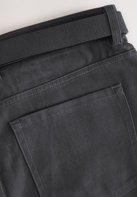 Czarne spodnie z tkaniny z teksturowanym pasem, prostym przeszyciem i jedną tylną kieszenią. Gładkie wykończenie materiału, trwała konstrukcja.