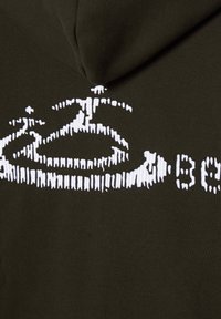 Olijfgroene hoodie met grote witte grafische tekstontwerpen op de achterkant, met een zachte structuur en een aangehechte capuchon.