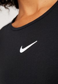 Persona che indossa una maglietta sportiva nera con il logo Nike bianco visibile sulla parte superiore del petto, vicino al collo.