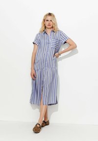 Robe rayée en tissu bleu clair et blanc, avec un design à boutonnière, une poche, des manches courtes et une jupe à volants. Associée à des chaussures à imprimé léopard.