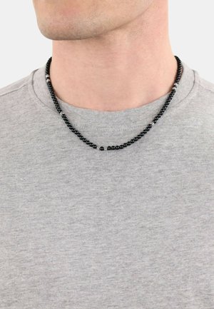 Black beaded necklace with metallic accents, displayed on a gray shirt. The beads vary in size, creating a textured, layered look.