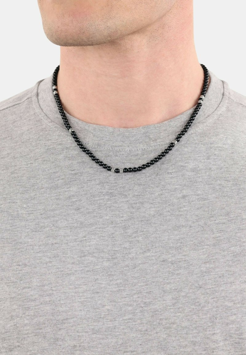 Zwarte kraalhalsketting met metallic accenten, tentoongesteld op een grijs shirt. De kralen variëren in grootte, waardoor een gestructureerde, gelaagde uitstraling ontstaat.