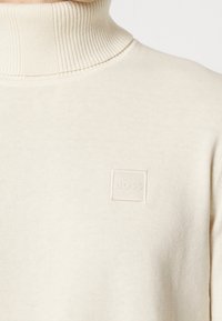 Krämfärgad ribbad polotröja med en liten broderad fyrkantig patch som har ordet "BOSS" på bröstet.