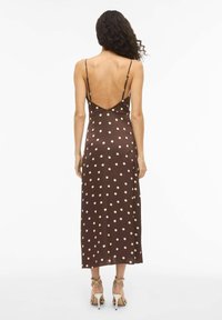 Smeđa midi haljina s točkicama, s dubokim V-izrezom na leđima, tankim podesivim trakama i glatkom teksturom. Kroja u obliku slova A, duga do sredine lista.