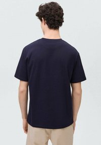 Temno modra bombažna majica s kratkimi rokavi, ravnega kroja in subtilnim embosiranim logotipom na hrbtni strani blizu ovratnika.