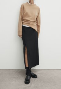 Beige oversized tröja med rundad halsringning, matchad med en svart midi kjol med en sidosprund. Svarta loafers och strumpor fulländar looken.