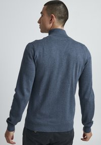 Mørkeblå strikkegenser med høy krage, ribbestrikkede mansjetter og kant, med en jevn tekstur og slim fit-design.