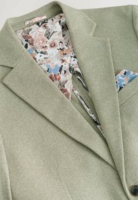 Hellgrüner strukturierter Blazer mit einem gefütterten Innenfutter im Blumenmuster; verfügt über aufgeschlitzte Revers und ein Einstecktuch in Blau- und Pfirsichtönen.