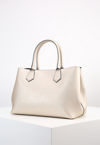 Beige syntetisk tote-väska med texturerad yta, med två korta handtag, en strukturerad form och svart kontrastsöm.