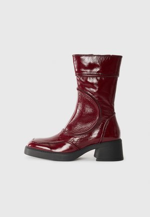 Burgundy glossy leather ankle boot with a rounded toe, textured finish, and a chunky black heel, featuring stitched detailing along the sides.