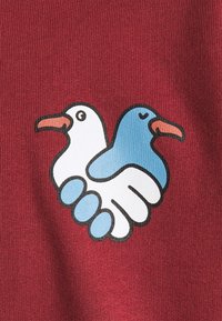 Kastanienbrauner Stoff mit einer Grafik von zwei stilisierten Vögeln, die sich die Flügel schütteln, einer weiß und einer blau, mit konturierten Details und einfarbigen Flächen.