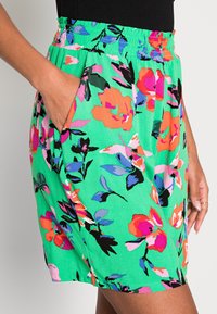 Un short floral en tissu vert avec un imprimé vibrant de fleurs roses, oranges et bleues. Taille élastique avec poches latérales.