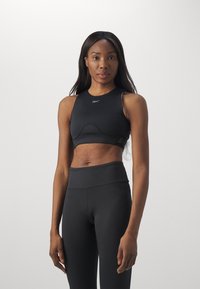 Črn atletski crop top z okroglim izrezom, ki se ponaša s sleek tkanino, konturnimi šivi in logotipom na sredini. V kombinaciji z visokimi črnimi legicami.