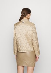 Beige quilted jacket with a shiny finish, featuring a collar and a small black logo on the back. Smooth texture and fitted design.