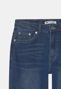 Vaqueros de mezclilla azul oscuro con una cintura de altura media, bolsillos frontales, costuras de color cobre y cierre de botón plateado. Presenta una etiqueta que dice "Levi's Mini Mon."