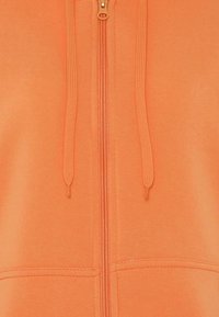 Orange zip-hættetrøje lavet af blødt stof, med en central lynlås, snore og syede detaljer foran.