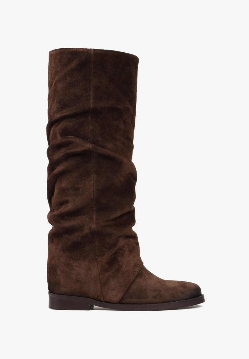 Brązowe zamszowe kozaki do kolan o luźnym fasonie, zaokrąglonym nosku i niskim, solidnym obcasie. Posiadają gładką teksturę i minimalne detale ściegów.