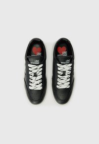 Zwarte leren sneakers met geperforeerde neus, wit- en zwartgestreepte veters en rode hartgraphics op de binnenzolen. Bevat "LOVE MOSCHINO" branding.