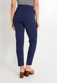 Pantalones ajustados de color azul marino con una cinturilla alta, que cuentan con bolsillos laterales y una textura suave. Combinados con sandalias marrones de tacón grueso.
