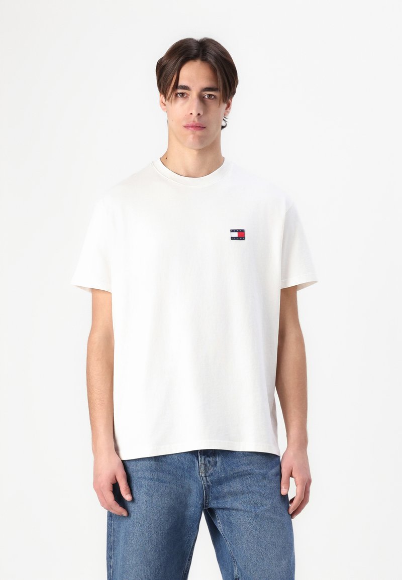 Tricou alb din bumbac, cu decolteu rotund și mâneci scurte. Prezintă un logo mic roșu, albastru și alb pe partea stângă a pieptului.