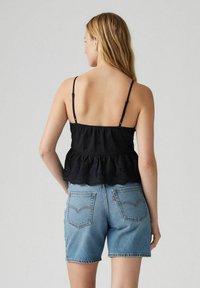 Top in peplo nero con spalline regolabili, caratterizzato da dettagli ricamati, abbinato a pantaloni corti in denim azzurro chiaro.
