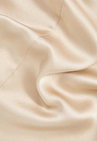 Tissu satin beige lisse et brillant avec des plis doux et des reflets lumineux créant une texture fluide et luxueuse.