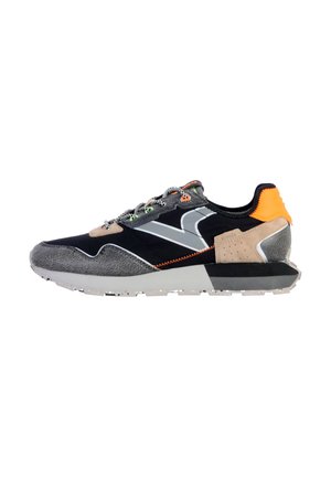 Zapatillas con una parte superior en negro y gris, que presentan una combinación de texturas, acentos naranjas, detalles reflectantes y una suela de goma blanca.