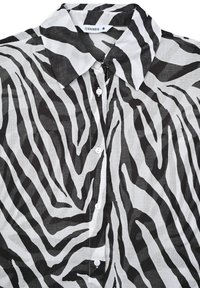 Camicia a fantasia zebra bianca e nera con colletto a bottoni, caratterizzata da un morbido tessuto e bottoni bianchi. Etichetta con la scritta "Terranova".