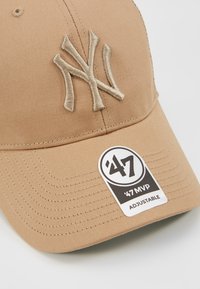 Justerbar tan baseballkappe med beige broderet NY-logo, buet skygge vendt fremad, og et mærke med teksten '47 MVP' på siden.