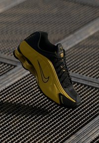 Svart och gul Nike löparsko med synlig logotyp, svarta snören och dämpad sula placerad på en metallgaller yta.