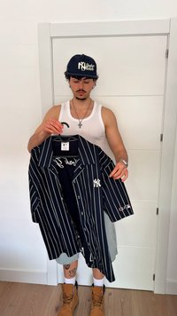 Sötétkék, csíkos ing fehér csíkokkal, rövid ujjal és hímzett NY logóval. Egy illő sötétkék sapka is látható.