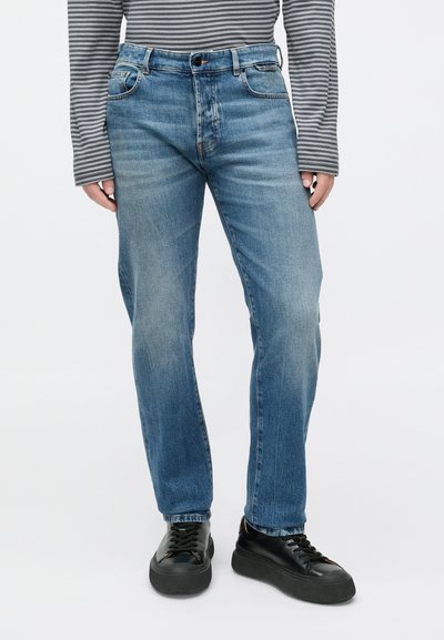 Τζιν παντελόνι σε ανοιχτό μπλε με άνετη εφαρμογή, διαθέτει πέντε τσέπες, θηλιές για ζώνη και ξεθωριασμένο τελείωμα, σε συνδυασμό με μαύρα αθλητικά παπούτσια.